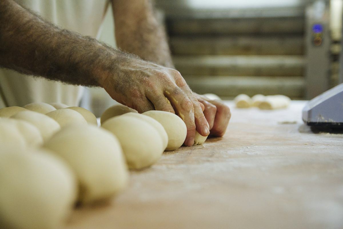 Een bakker vormt bolletjes deeg op een werkbank met bloem